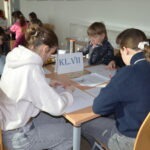 Uczniowie siedzą przy stole w bibliotece, pracując nad zadaniami z materiałami edukacyjnymi.