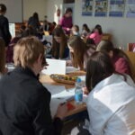 Uczniowie siedzą przy stolikach podczas zajęć w bibliotece szkolnej.