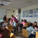 Uczniowie siedzą przy stolikach podczas zajęć w bibliotece szkolnej.