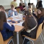 Uczniowie siedzą przy stole w bibliotece, pracując nad zadaniami związanymi z językiem polskim.