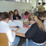 Uczniowie siedzą przy stole w bibliotece, pracując nad zadaniami związanymi z językiem polskim.