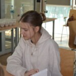 Dziewczynka siedzi przy stole w bibliotece, trzymając kartkę papieru.