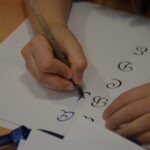 Dziecko piórem z atramentem ćwiczy kaligrafię na papierze.