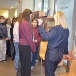 Uczniowie obserwują bibliotekarkę podczas demonstracji poszukiwania książek na półkach.