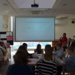 Uczniowie siedzą w sali lekcyjnej podczas prezentacji wyświetlanej na ekranie z projektorem.