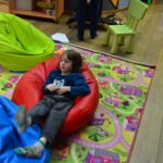 Chłopiec siedzi na czerwonym worku sensorycznym na kolorowej macie w sali zabaw.