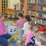 Dzieci słuchają nauczycielki podczas zajęć edukacyjnych w bibliotece.