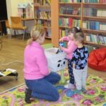 Kobieta siedzi na podłodze, a obok niej dwójka dzieci dotyka woreczka sensorycznego.