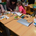 Dziecko siedzące przy stole koloruje rysunek kredkami podczas zajęć z Dyskusyjnego Klubu Książki dla dzieci.