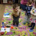 Dzieci bawią się na kolorowej macie, otoczone edukacyjnymi materiałami związanymi z higieną jamy ustnej.