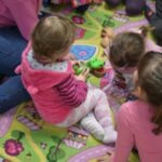 Dziecko w różowym sweterku bawi się klockami na kolorowej macie.
