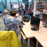 Uczestnik warsztatów siedzi przed komputerem, skierowany tyłem do prowadzącego i prezentacji wyświetlanej na ekranie.