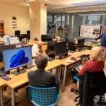 Uczestnicy warsztatów z zakresu bankowości elektronicznej pracują przy komputerach, podczas gdy prowadzący prezentuje informacje na tablicy.