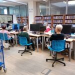 Uczestnicy warsztatów siedzą przy komputerach w bibliotece, korzystając z zasobów i wsparcia doradcy kariery.
