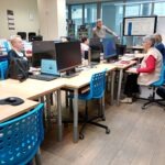 Uczestnicy warsztatów korzystają z komputerów i monitorów podczas spotkania w bibliotece.